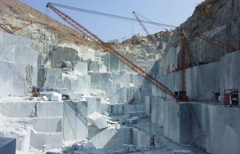 Natural stone quarrying and block extraction operations by Indian Natural Stones, showcasing large-scale stone mining and crane handling at the quarry site