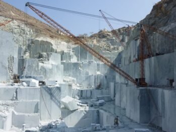 Natural stone quarrying and block extraction operations by Indian Natural Stones, showcasing large-scale stone mining and crane handling at the quarry site