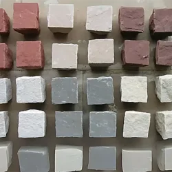 Assorted sandstone cobblestone blocks in multiple colors and finishes displayed in rows by Indian Natural Stones.